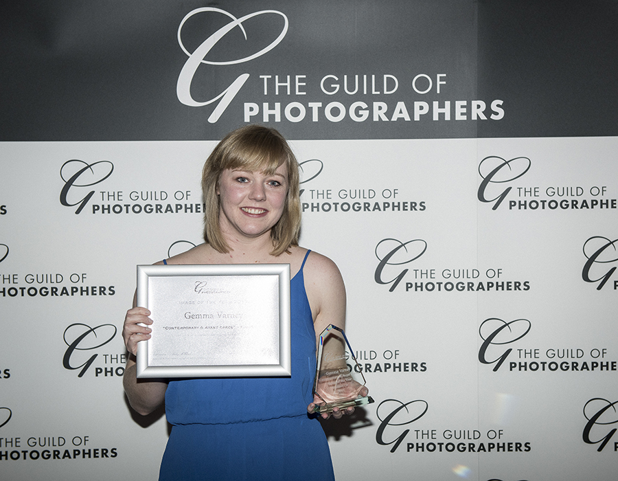 Gem holding her award from the guild of photographers in front of a branded wall